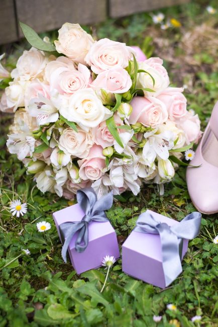 A floral arrangement featuring a bouquet of white and pale pink roses, complemented by white alstroemeria with pink streaks and green foliage, displayed on a grassy surface with small white and yellow